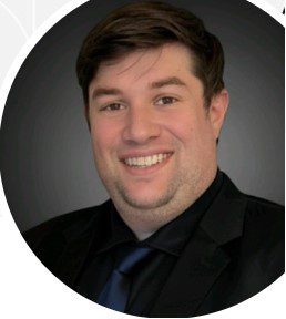 Professional headshot of a smiling man in a black suit and blue tie.