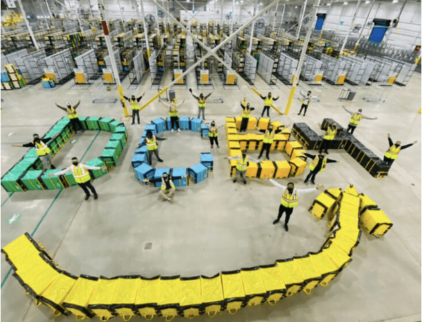 Workers form the word "OPENAI" with colorful packages in a warehouse.