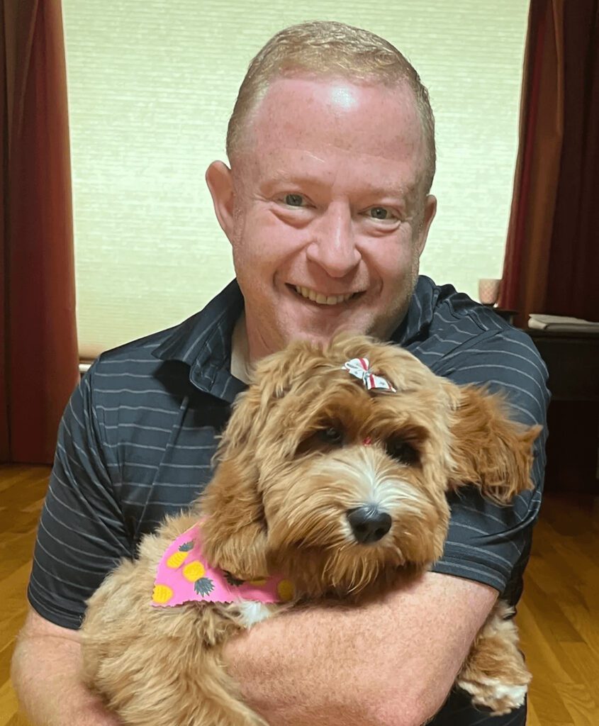 Man happily holding a small brown dog.
