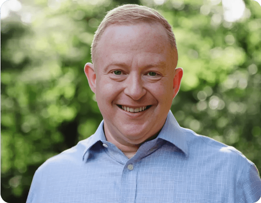 Smiling person in blue shirt, green background.